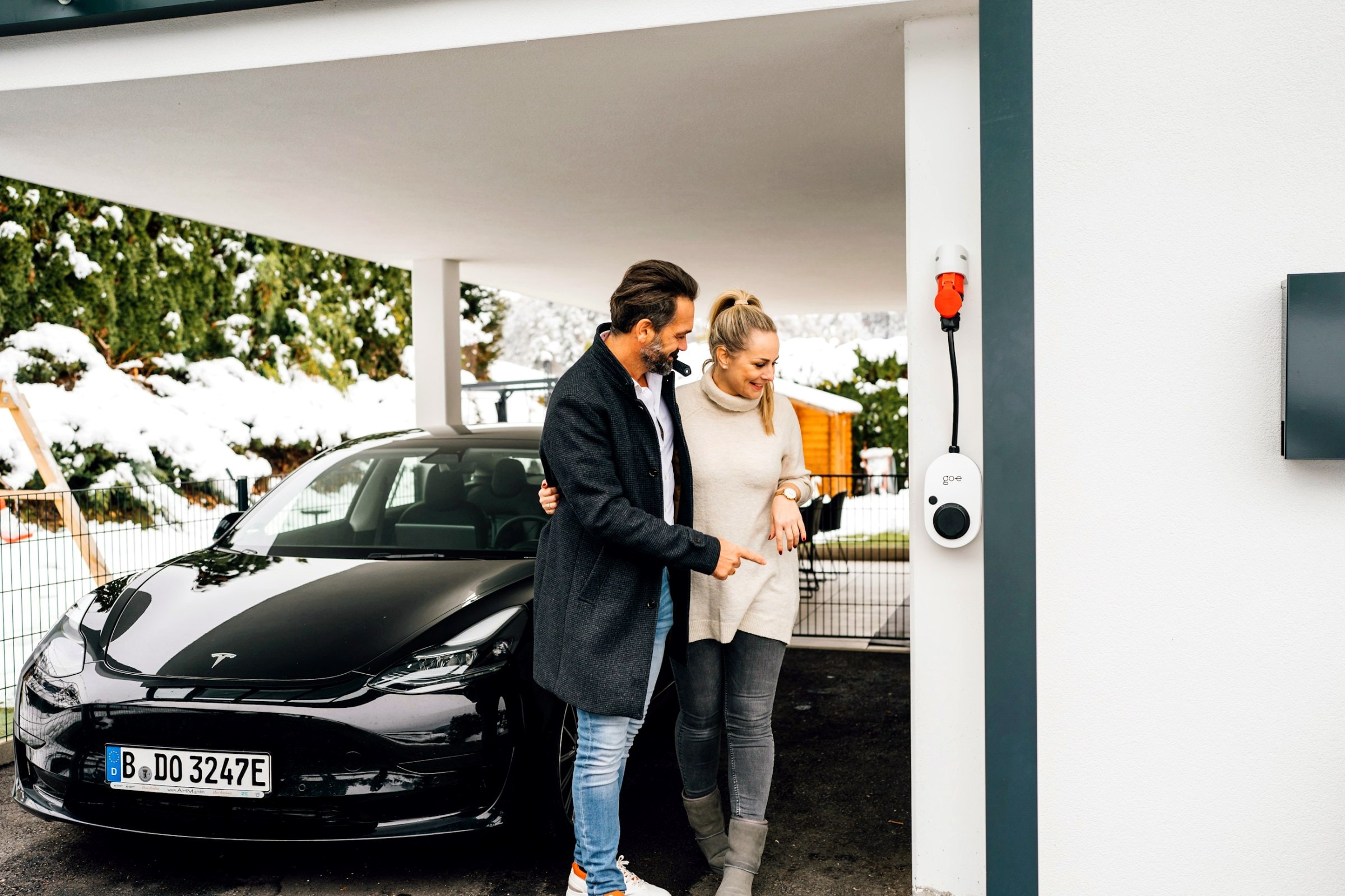 Paar am Carport, das E-Auto lädt an der Wallbox