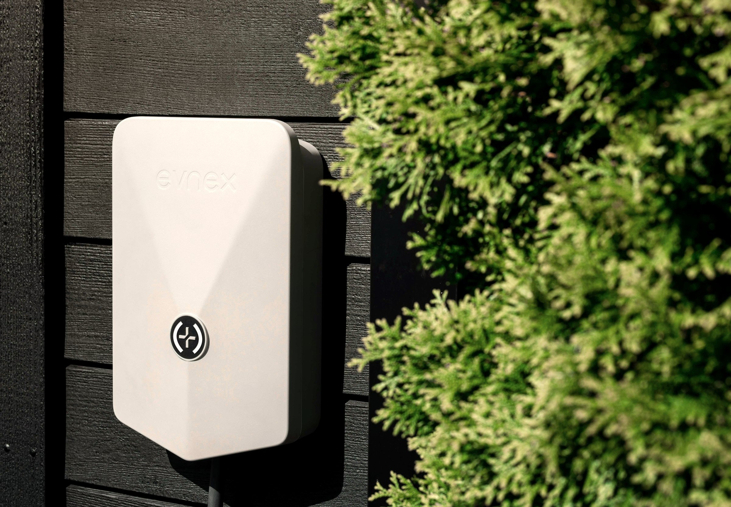Wallbox an der Hauswand neben einer Hecke