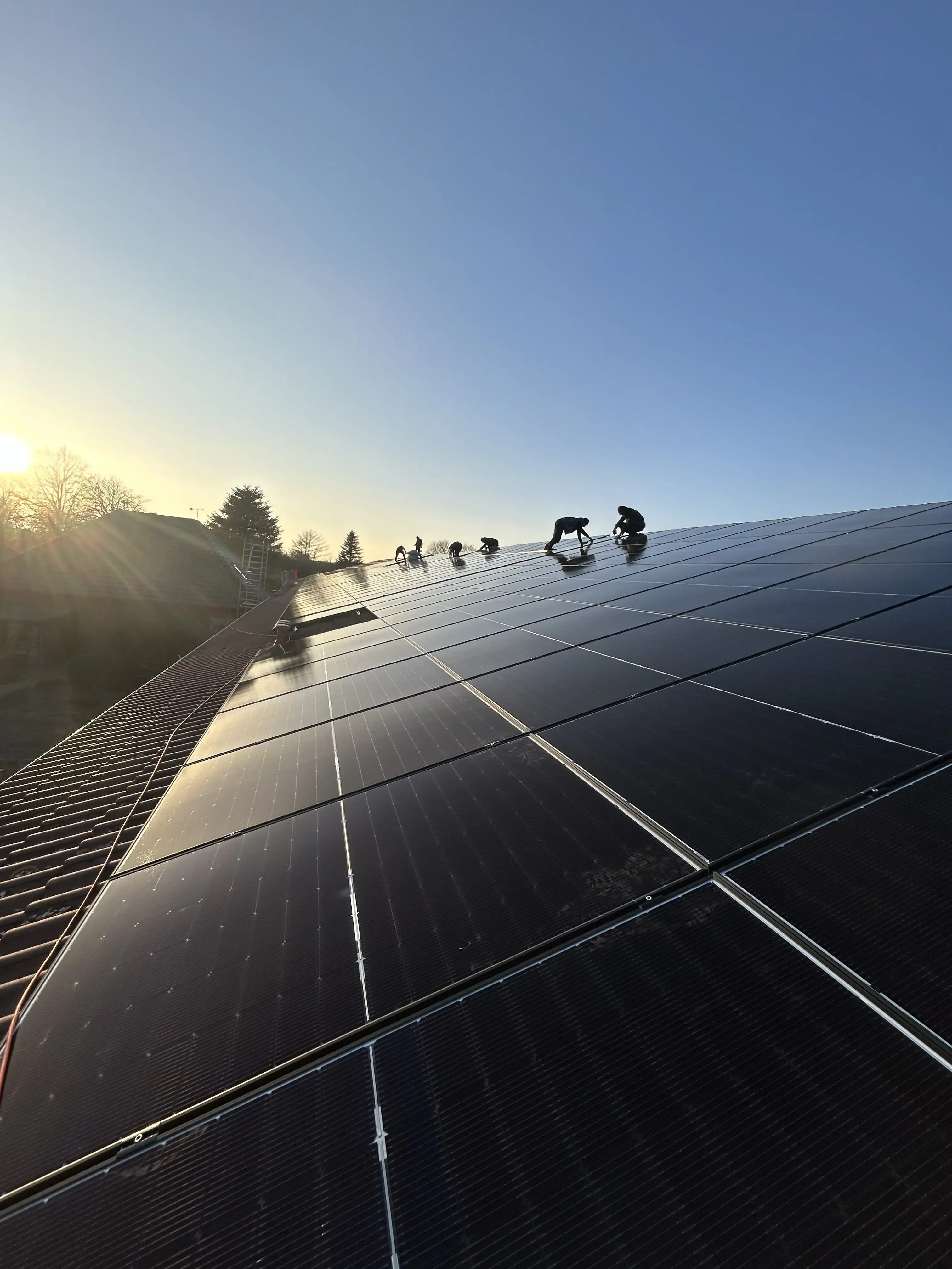 Monteure installieren Photovoltaikanlage auf großem Dach bei Sonnenaufgang.