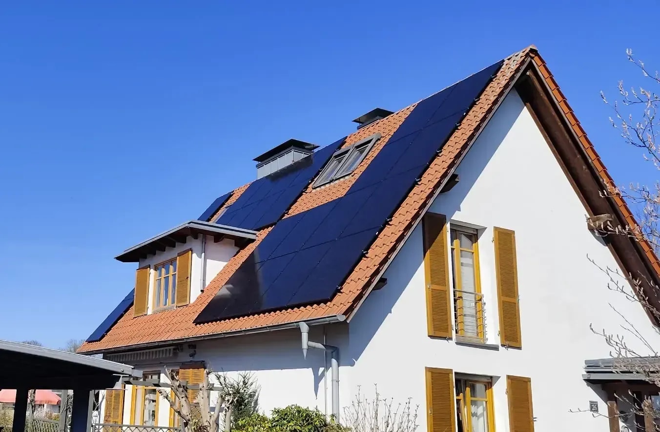 Einfamilienhaus mit Photovoltaikanlage auf dem Satteldach unter blauem Himmel.