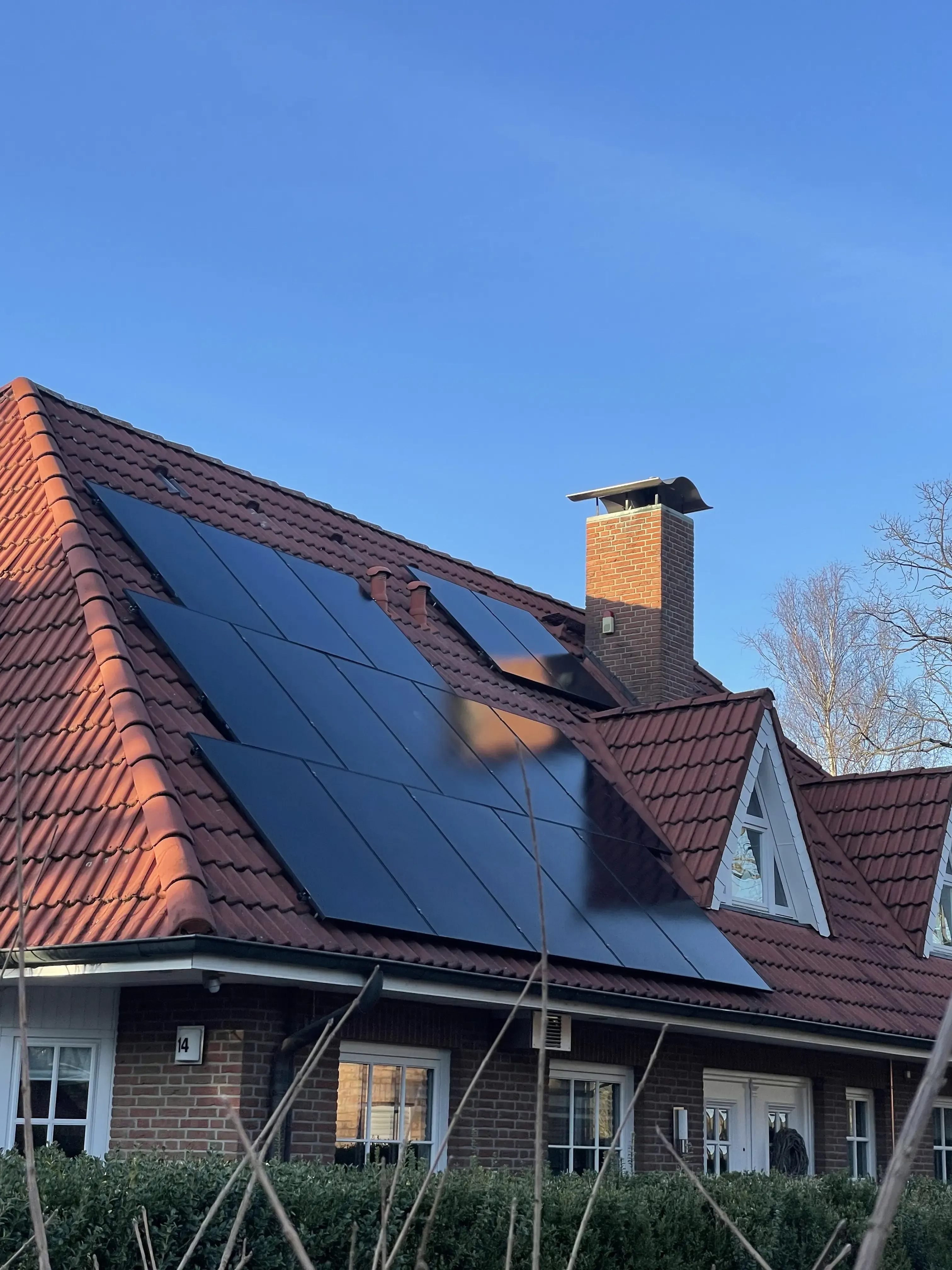 Photovoltaikanlage mit schwarzen Solarmodulen auf dem Ziegeldach eines Einfamilienhauses.